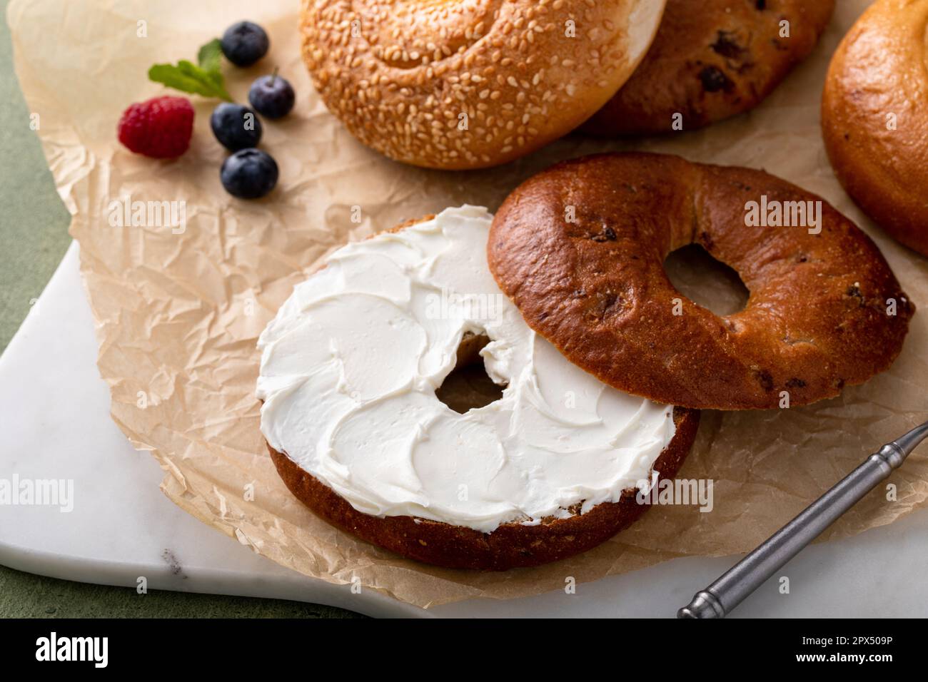 Bagels maison fraîchement cuits sur un papier parchemin prêt à manger, raisins secs de cannelle, sésame et bagel simple servi avec du fromage à la crème et des baies fraîches Banque D'Images