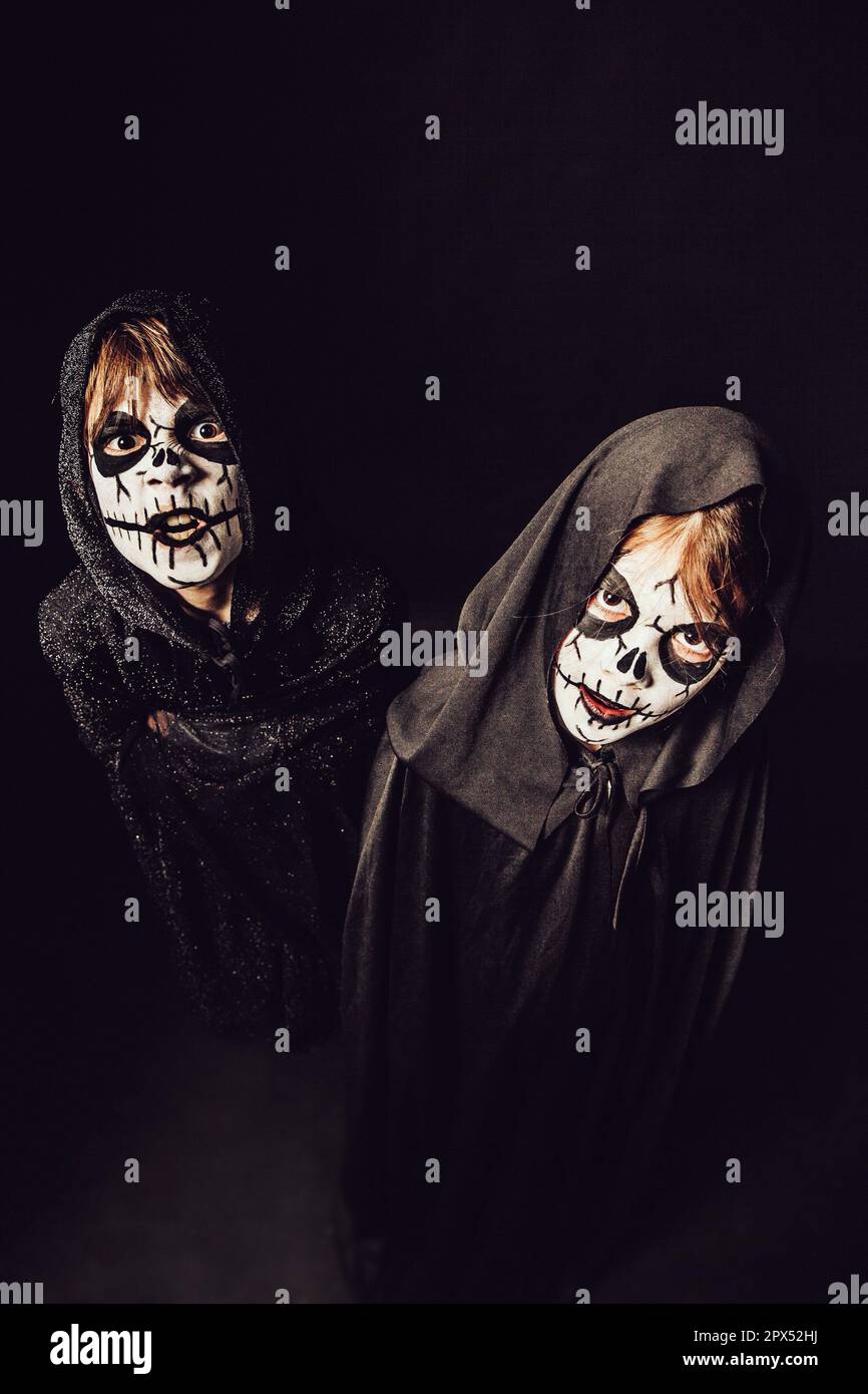 Deux enfants portent des robes sombres et de la peinture effrayante pour le visage à Halloween. Banque D'Images