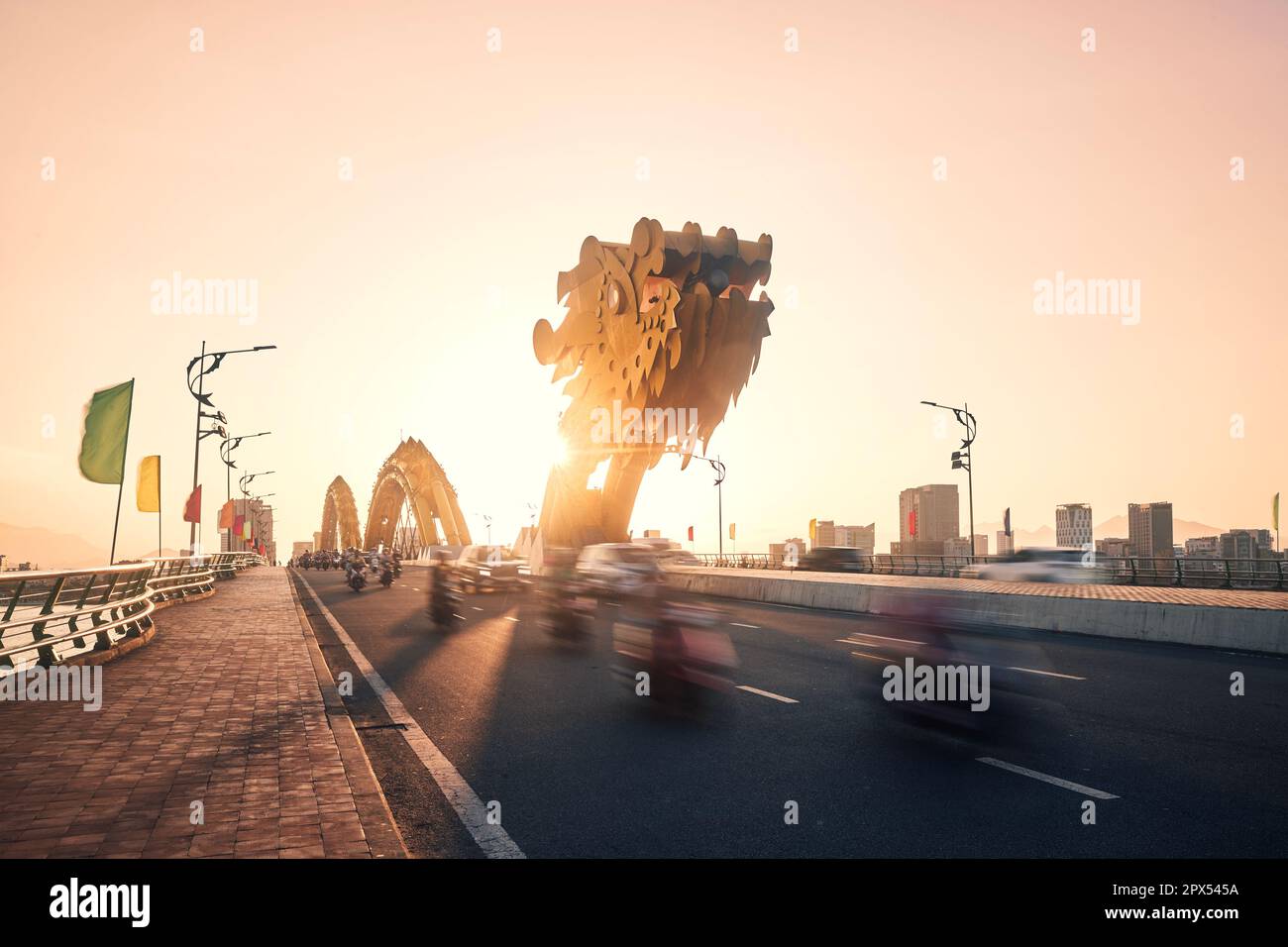 Trafic avec beaucoup de motos en mouvement flou sur le pont Dragon. Da Nang ville au coucher du soleil doré, Vietnam. Banque D'Images