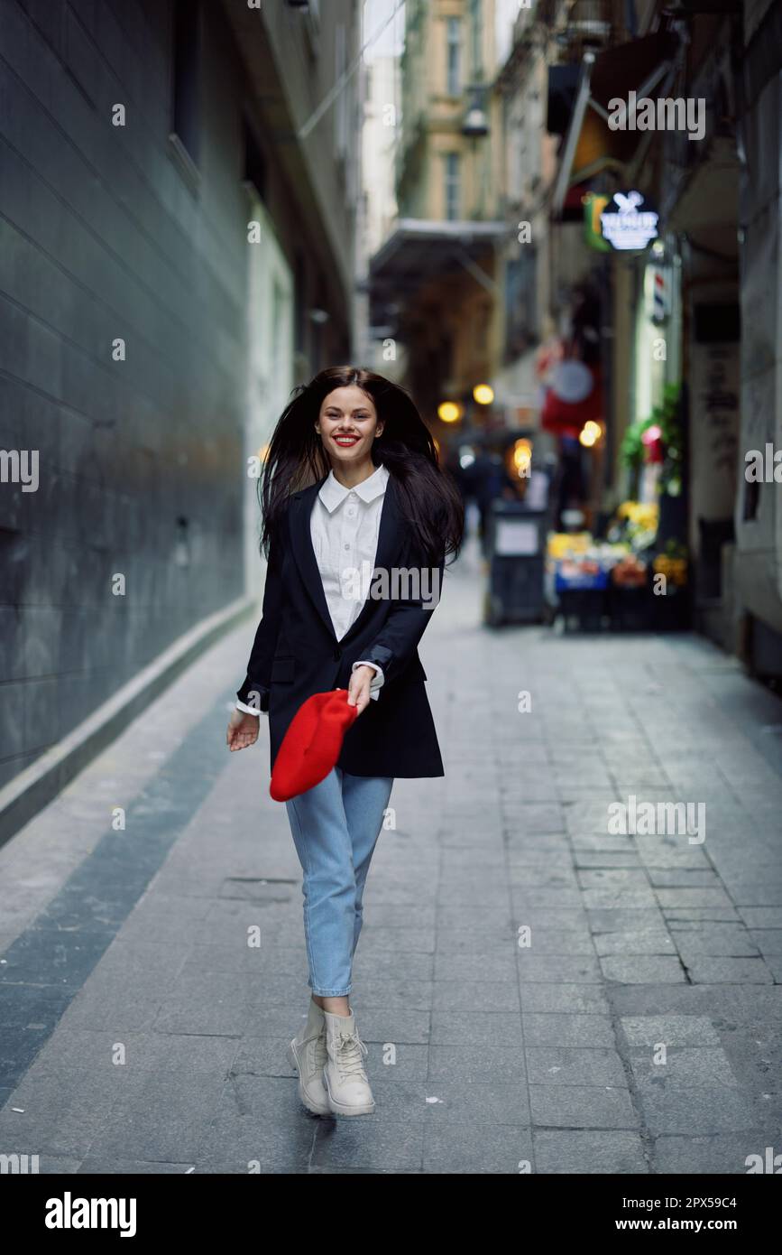 Femme de mode touriste dans des vêtements élégants dans une veste et béret  rouge courant le long de la rue étroite de la ville sourire et le voyage du  bonheur, style français