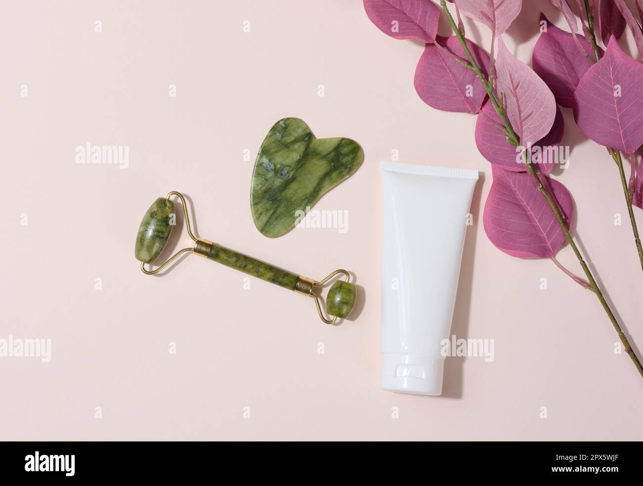 Masseur facial manuel Jade et tubes en plastique blanc pour cosmétiques sur fond beige, vue du dessus Banque D'Images