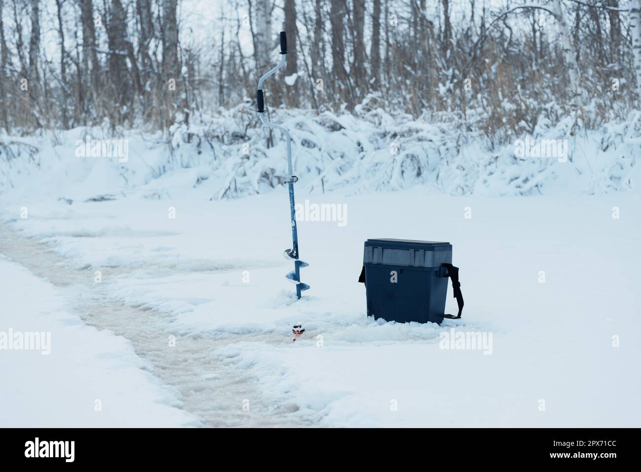 Boîte à pêche, canne à pêche et exercice sur glace près du trou sur la glace en hiver Banque D'Images