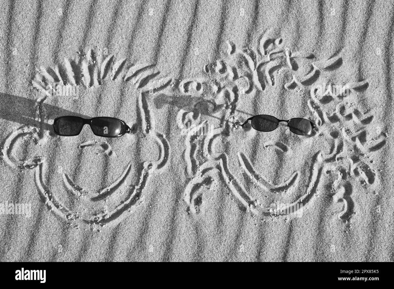 Visage dessiné dans le sable sur la plage, avec des lunettes de soleil. Poncer avec motif ondulé. Photo de vacances primal de la mer Banque D'Images