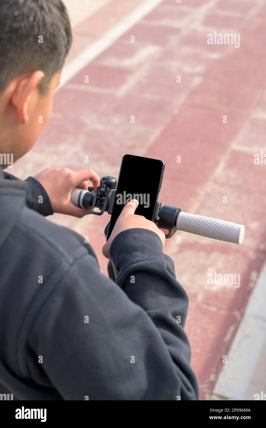 Jeune homme à bord d'un scooter électrique en plein air, regardant l'itinéraire sur l'application de carte de smartphone, concept de transport durable, zéro CO2 émission vert Banque D'Images