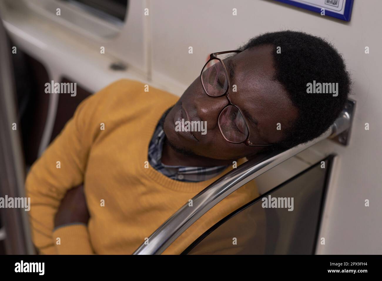 Jeune homme fatigué en lunettes dormant en voiture de métro pendant son voyage Banque D'Images