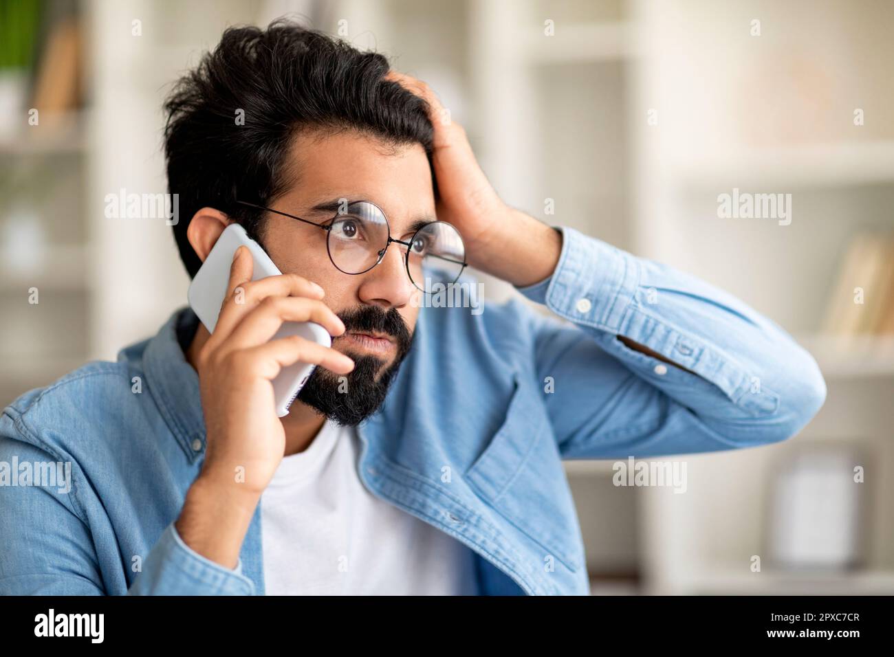 A souligné le jeune Indien Guy en lunettes de vue parlant sur le téléphone cellulaire et touchant la tête Banque D'Images