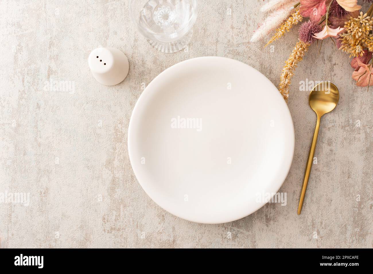 Table, assiette et couverts dorés sur fond marron, verre à vin vide, vue sur le dessus de la table servie décorée de fleurs sèches Banque D'Images