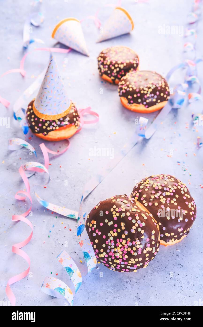 Pâtisserie berlinère au chocolat pour le carnaval et la fête. Krapfen allemand ou beignets avec des banderoles et des confettis. Image de carnaval ou d'anniversaire colorée Banque D'Images