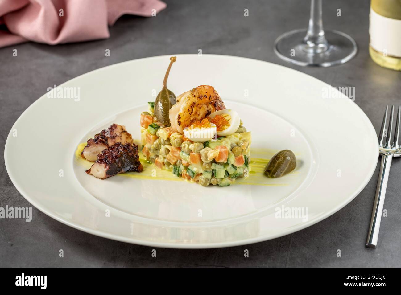 Salade russe à la sauce aioli, crevettes, poulpes et câpres sur une assiette en porcelaine blanche Banque D'Images