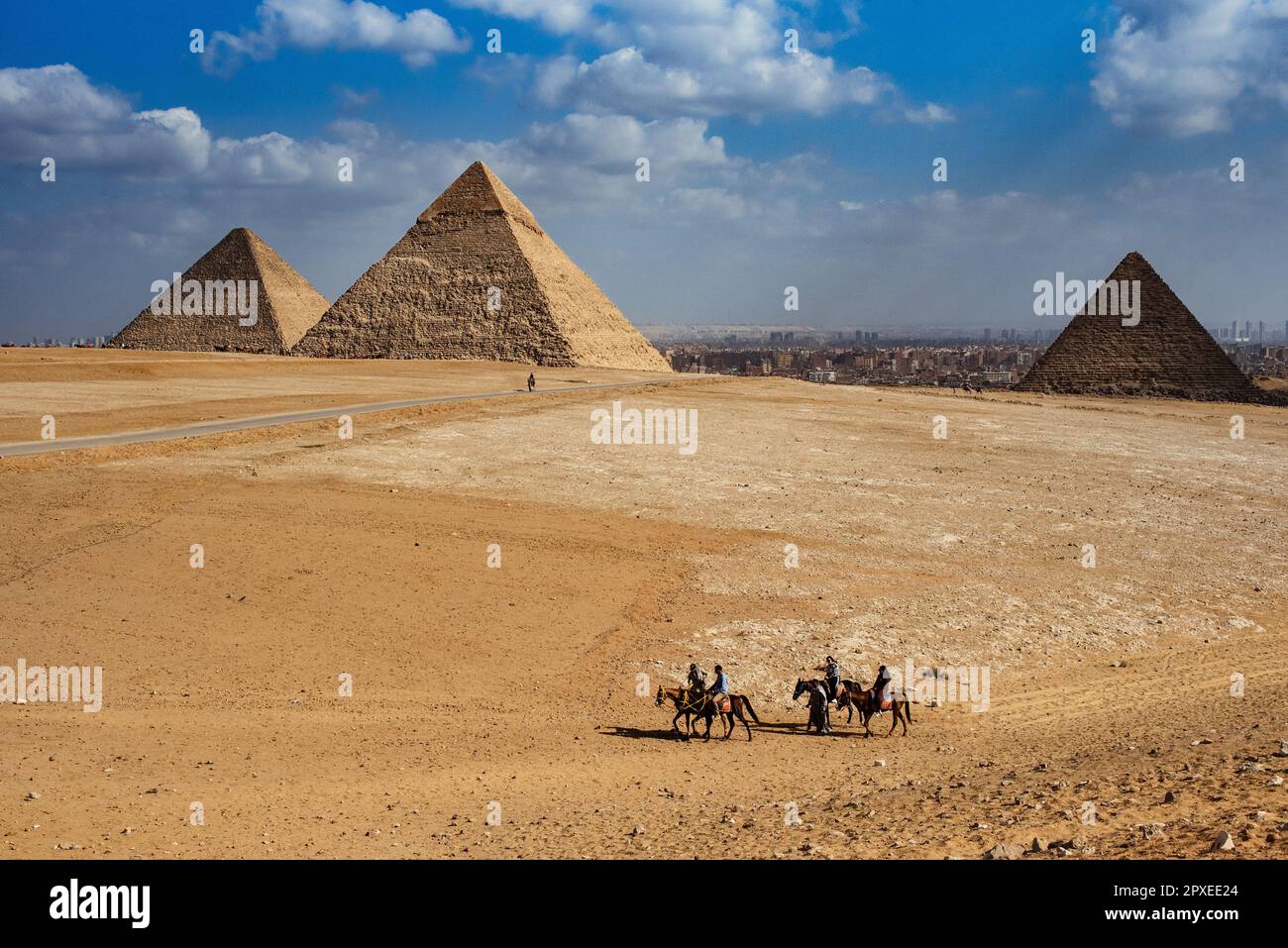 Quatre personnes à cheval sur un vaste paysage désertique, avec les majestueuses pyramides de Gizeh en arrière-plan Banque D'Images