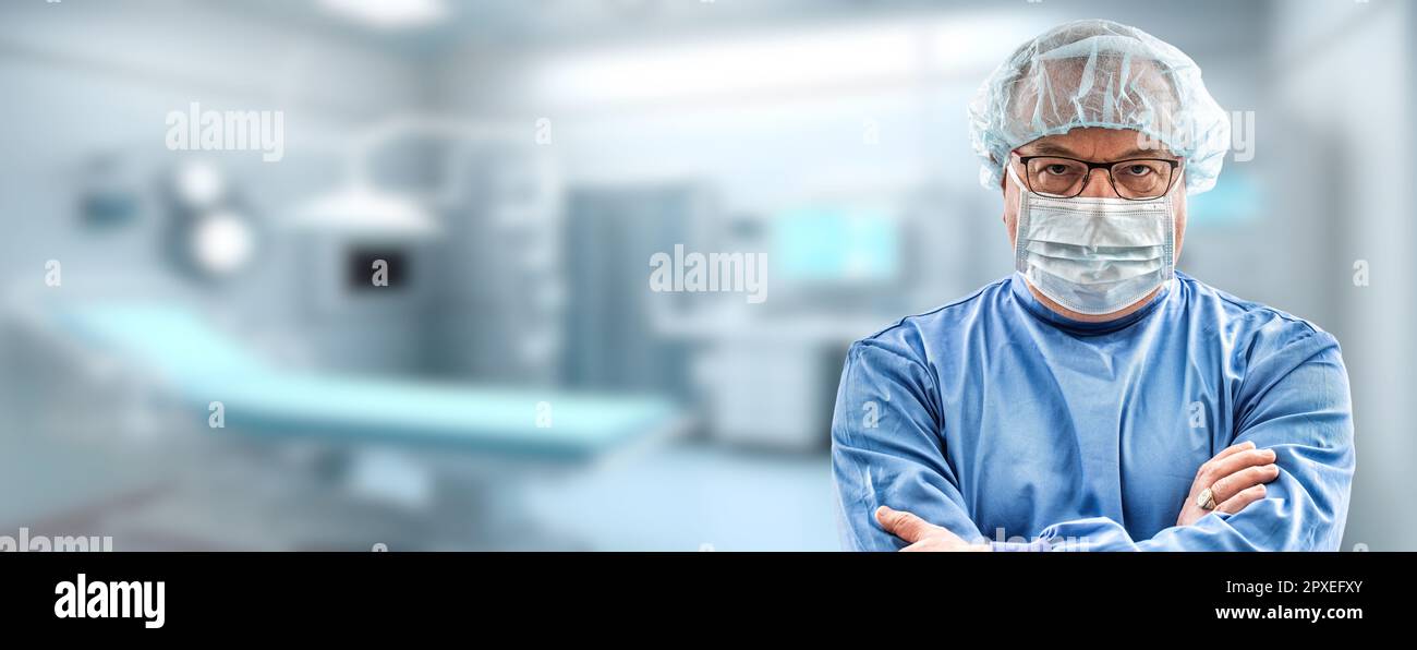 Un chirurgien expérimenté, portant un manteau de travail bleu et un masque de protection, se tient devant une salle chirurgicale floue. Banque D'Images