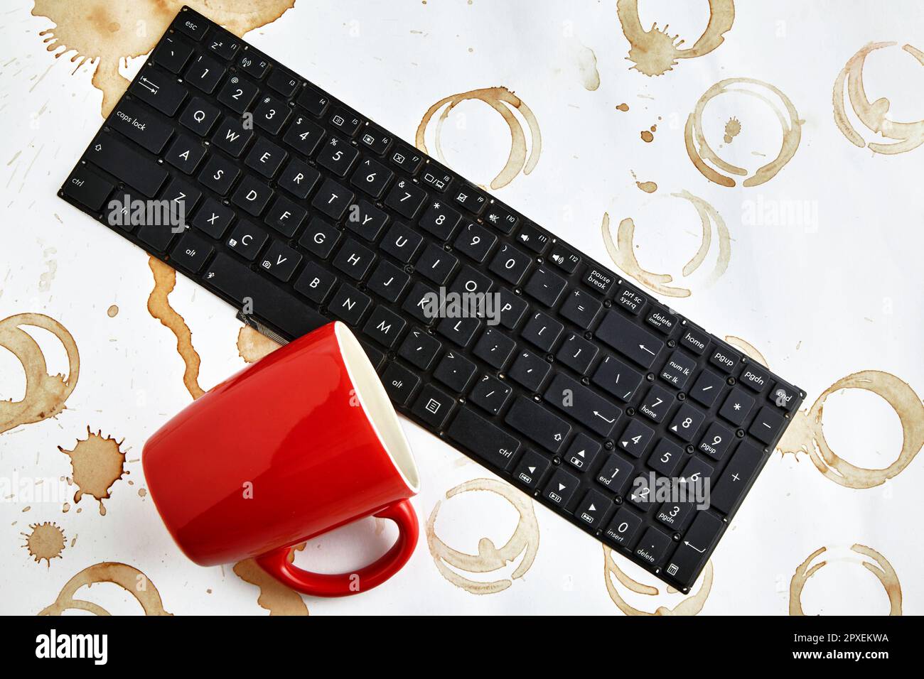 Tasse de café rouge renversée sur un clavier d'ordinateur sur une table avec des taches de café. Clavier rempli de boisson au café Banque D'Images Tasse de café rouge renversée sur un clavier d'ordinateur sur une table avec des taches de café. Clavier rempli de boisson au café Banque D'Images