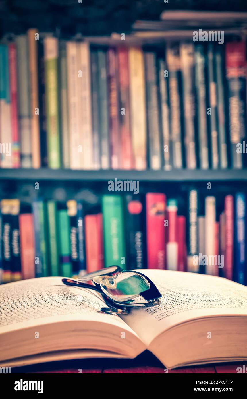 Ouvrez un livre et des lunettes avec des livres sur une étagère à l'arrière-plan. Thème de passer du temps libre approfondir vos connaissances. Photo avec une faible profondeur de vie Banque D'Images
