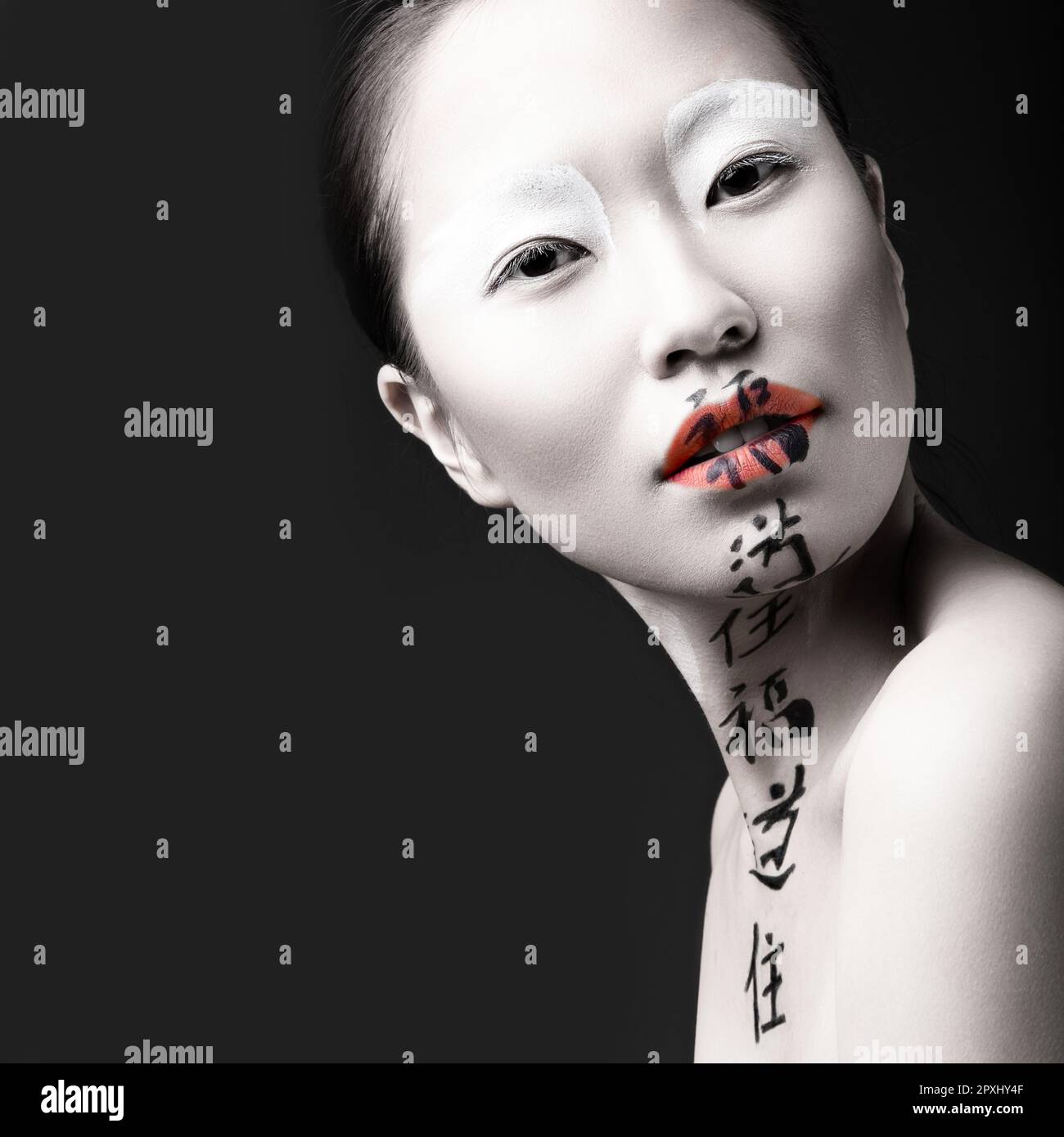 Belle fille asiatique avec peau blanche, lèvres rouges et hiéroglyphes sur son visage. Art Beauté image. Photo prise en studio sur fond noir. Banque D'Images