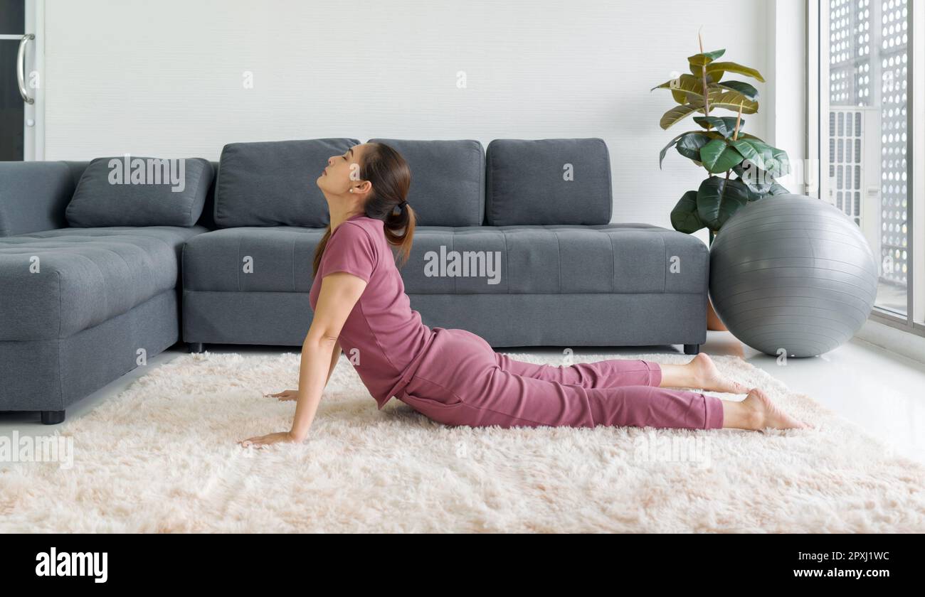 Femme au foyer asiatique faisant l'exercice de posture de Cobra pendant l'entraînement à la maison. Les femmes pratiquant le yoga à Bhujangasana posent sur la moquette dans le salon. Banque D'Images