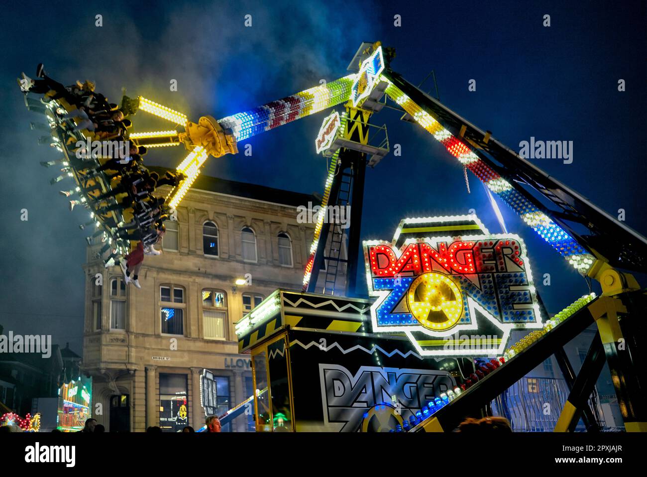 Frissons de foire, avec des gens hissés haut sur un bras de grue et tournés autour. Promenade nocturne à sensations fortes sur le terrain de foire. Angleterre Royaume-Uni Banque D'Images