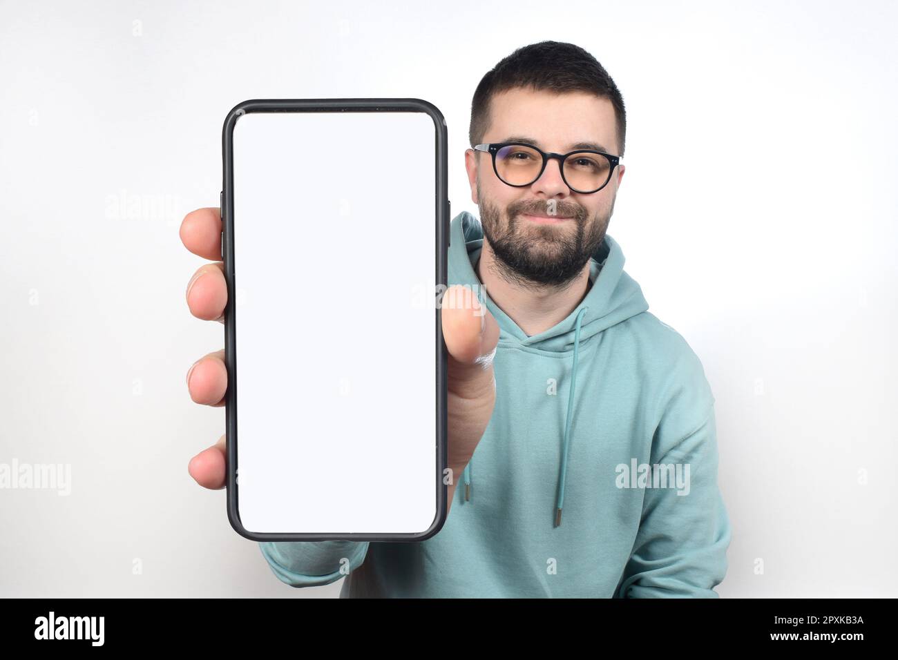 un jeune homme avec des lunettes et une barbe montre un téléphone avec un écran blanc vierge Banque D'Images