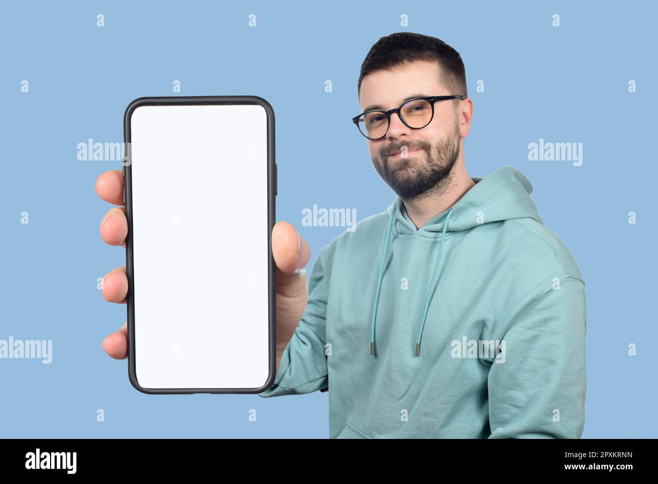un jeune homme avec des lunettes et une barbe montre un téléphone avec un écran blanc vierge Banque D'Images