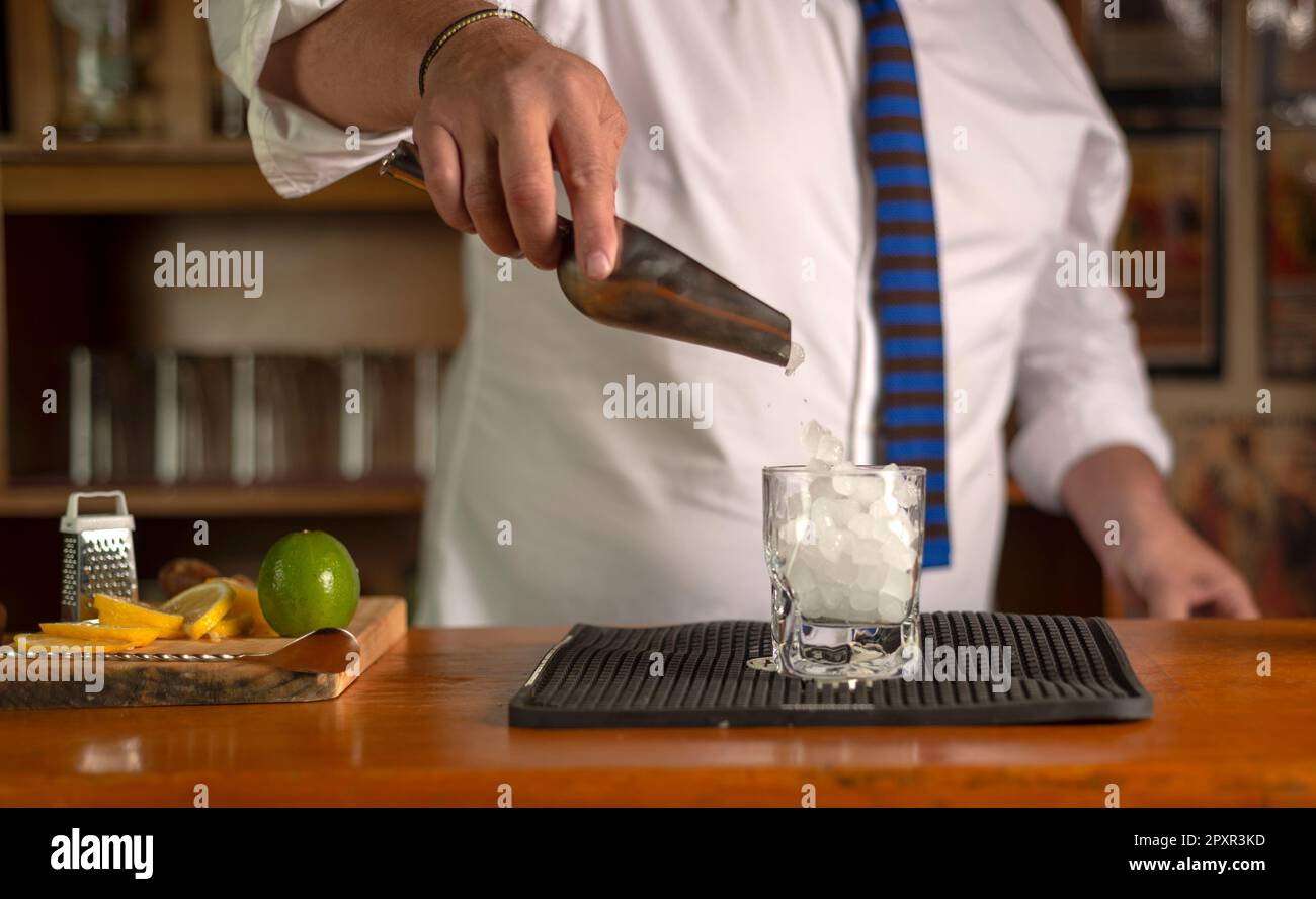le barman tient une cuillère en métal avec des glaçons dans sa main et les  verse dans un verre préparé pour faire un cocktail dans une boîte de nuit  Photo Stock 