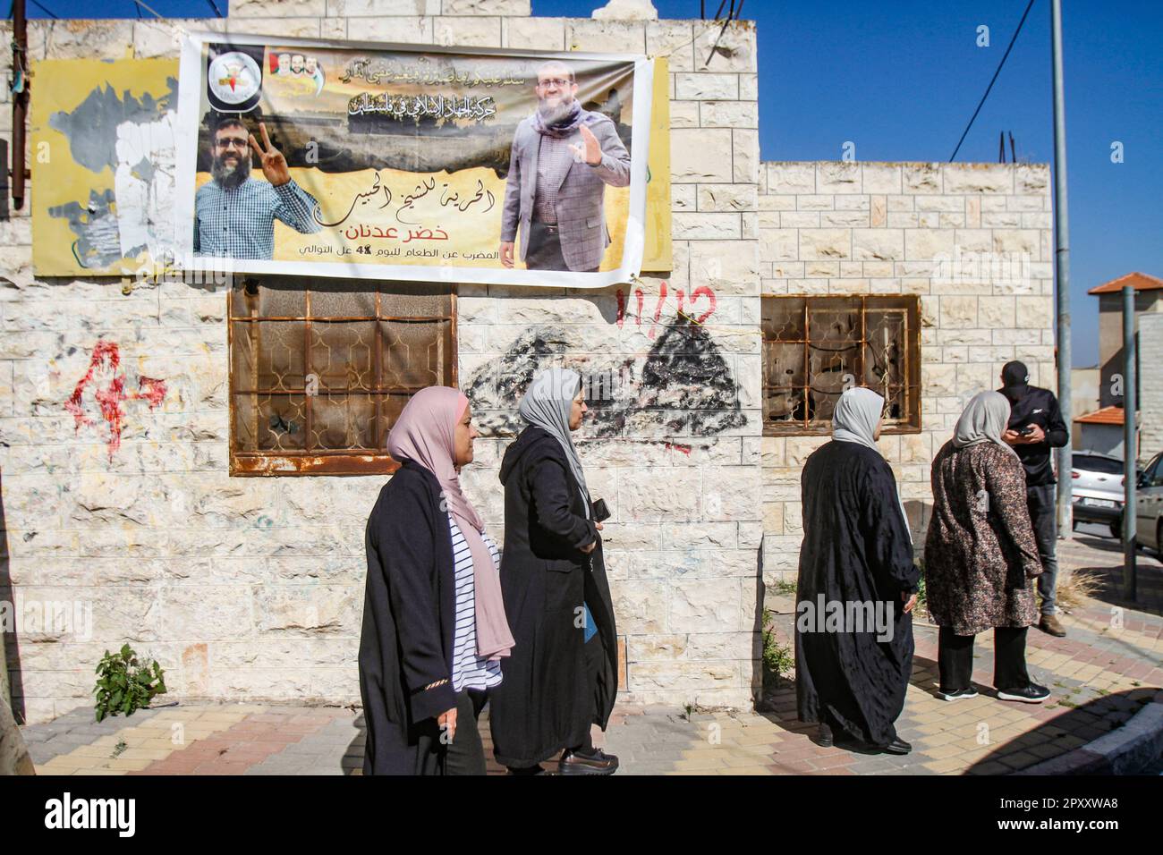 Une vue d'une affiche accrochée sur un mur de feu Khader Adnan palestinien, un activiste du mouvement Jihad islamique, à côté de lui sont voilées des femmes devant son domicile dans le village d'Arraba près de Jénine en Cisjordanie. Khader Adnan mort dans les prisons, après une grève de la faim qui a duré 87 jours. Le Premier ministre palestinien Muhammad Shtayyeh a déclaré que l'occupation avait commis un assassinat contre Adnan en refusant de demander sa libération et en le négligeant médicalement, et le ministère palestinien des Affaires étrangères a tenu le gouvernement israélien pleinement responsable du crime qui a conduit à la marty Banque D'Images