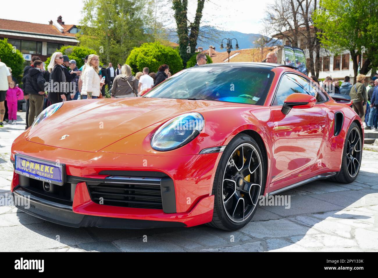 Une élégante voiture de sport rouge Porsche est garée sur une allée pavée, où les gens se rassemblent pour admirer son design élégant Banque D'Images