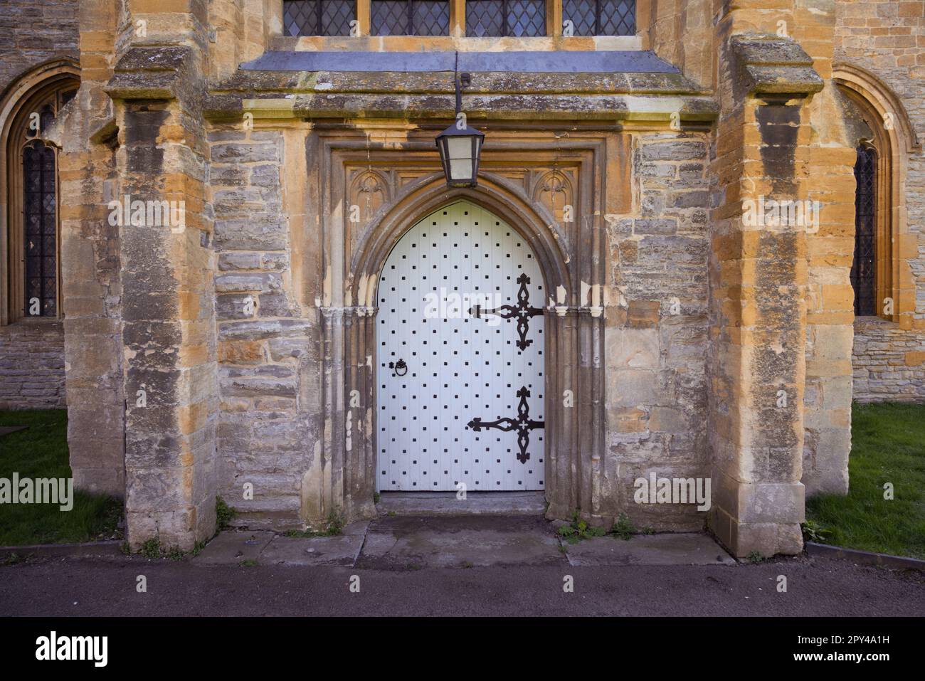 Une porte en bois robuste, peinte en blanc, avec de grandes charnières en métal très ouvrées dans une porte en pierre voûtée. Banque D'Images