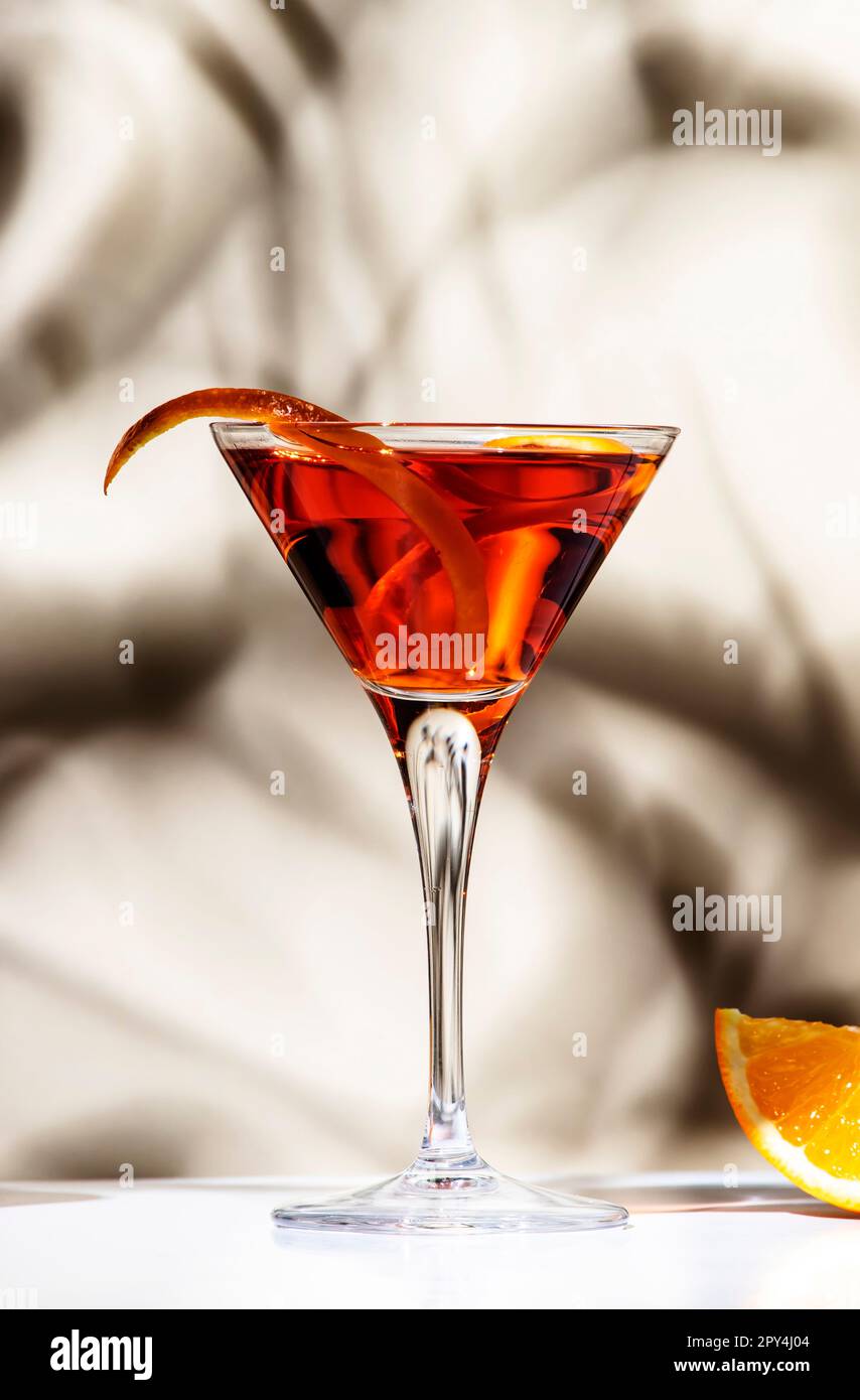 Cocktail d'orange Martinez avec vermouth rouge, liqueur, amer, zeste d'agrumes et glace en verre martini. Arrière-plan beige clair, lumière dure, ombre pa Banque D'Images