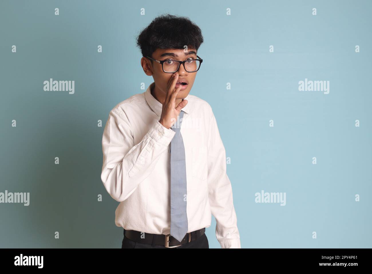 Élève de lycée indonésien portant un uniforme de chemise blanc avec une cravate grise pour murmurer une conversation malicieuse, main sur la bouche pour dire secret r Banque D'Images