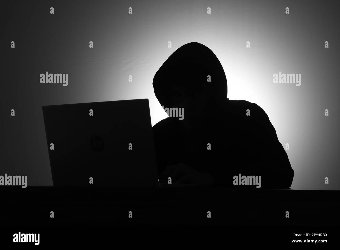 Mystérieux homme portant un sweat à capuche noir à l'aide d'un ordinateur portable et tenant une carte de crédit dans la pièce sombre. Concept de piratage et de cybersécurité. Banque D'Images