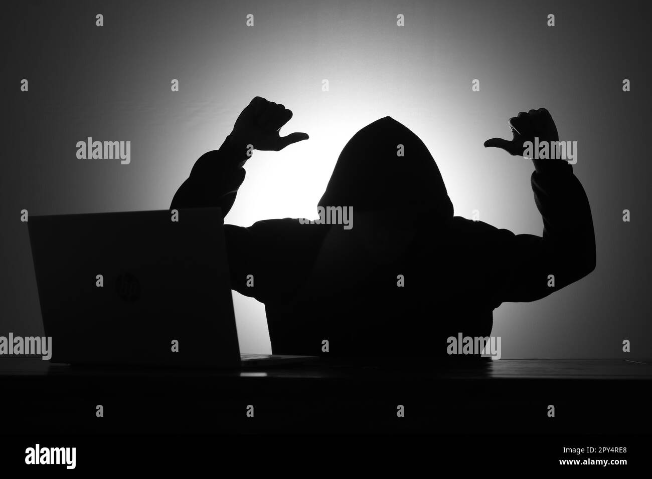 Mystérieux homme portant un sweat à capuche noir avec un ordinateur portable tout en moquant quelqu'un en faisant un geste du pouce vers le bas dans la pièce sombre. Hacker et cyber-sécurité concep Banque D'Images