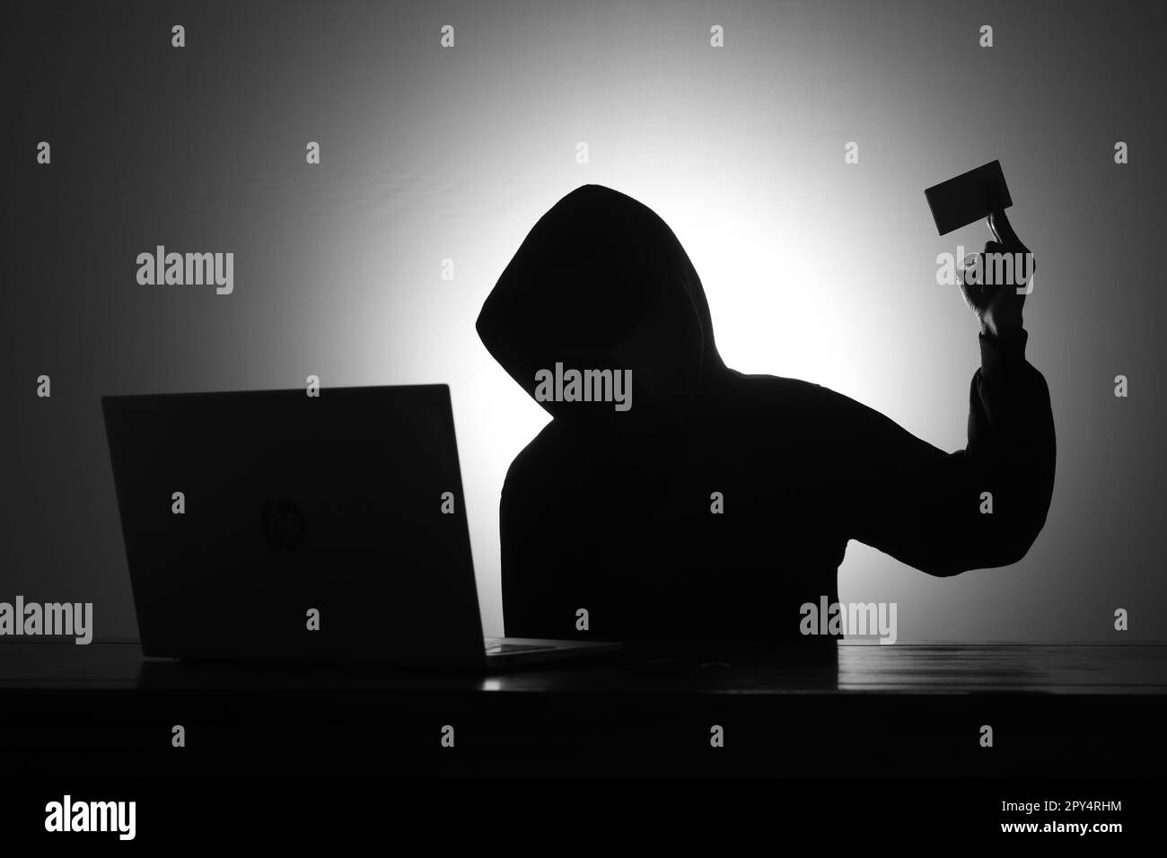 Mystérieux homme portant un sweat à capuche noir à l'aide d'un ordinateur portable et tenant une carte de crédit dans la pièce sombre. Concept de piratage et de cybersécurité. Banque D'Images