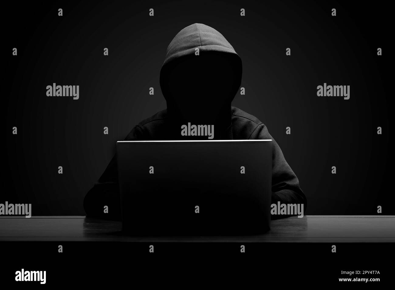 Mystérieux homme portant un sweat à capuche noir utilisant un ordinateur portable dans la pièce sombre. Concept de piratage et de cybersécurité. Banque D'Images