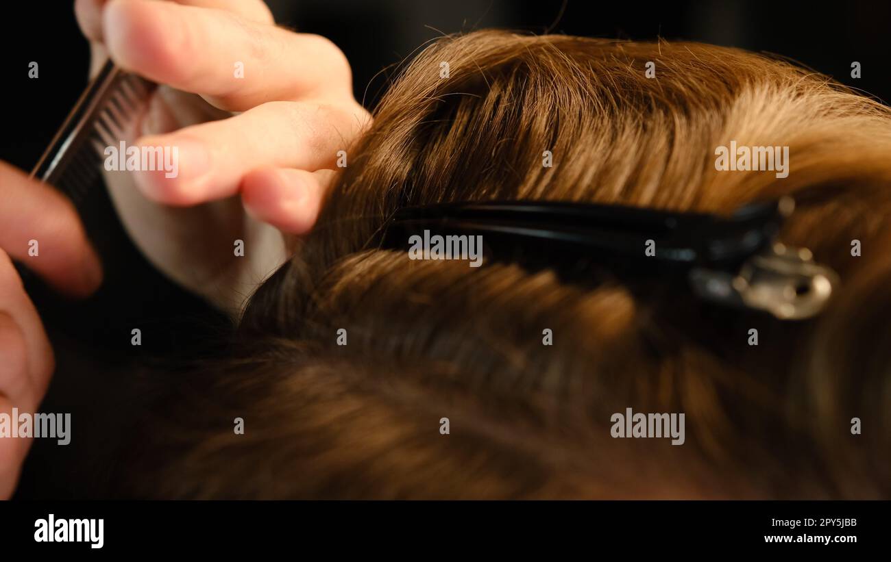 Gros plan du coiffeur à l'aide d'un clip pour fixer les cheveux pour les couper et les coiffer. Salon de coiffure Pinsn. service dans un salon de coiffure moderne dans un éclairage sombre avec une lumière chaleureuse vue arrière Banque D'Images
