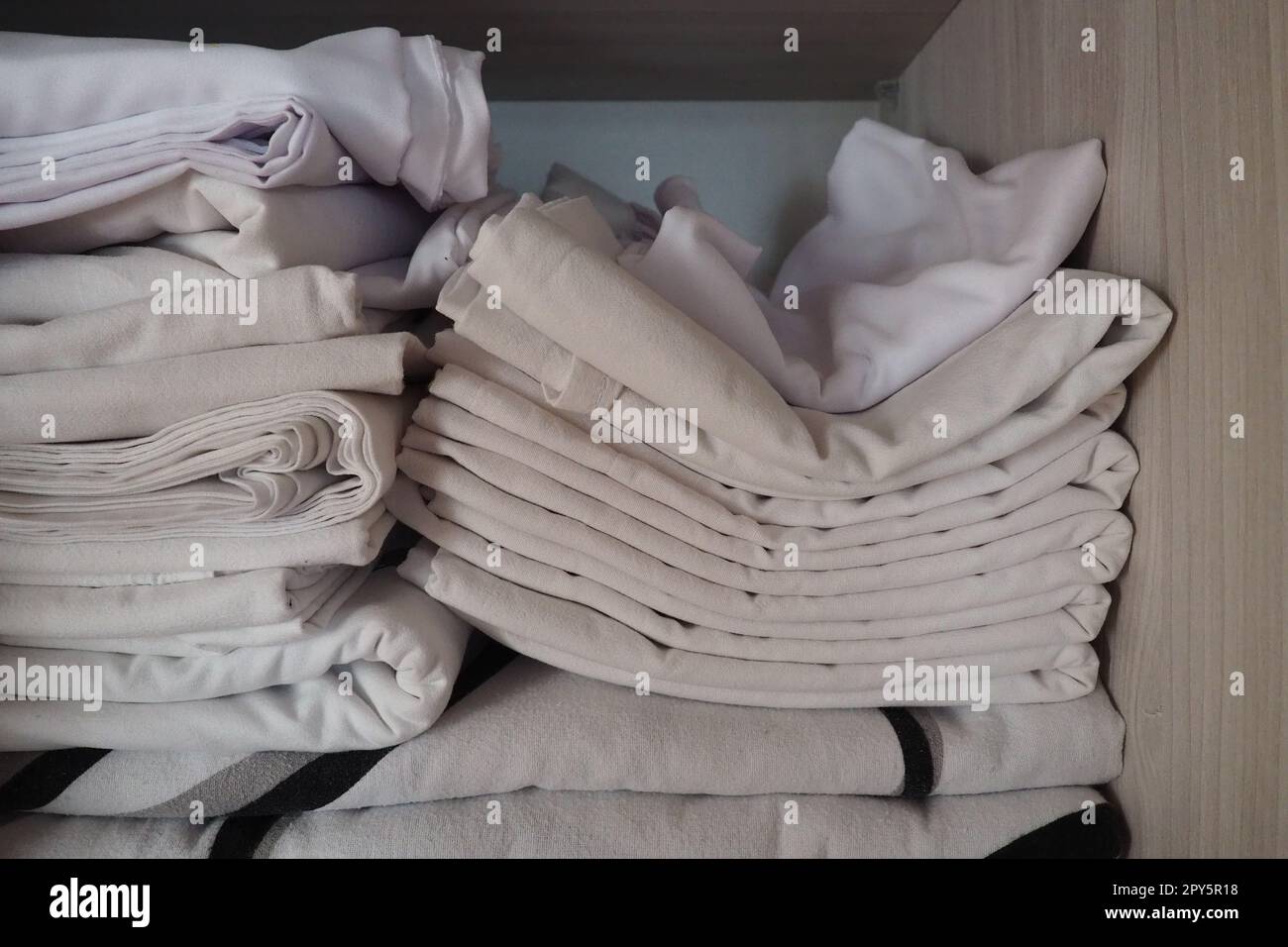 Les draps blancs sont empilés dans le placard. Contenu interne d'une armoire à linge. Organisation du ménage. Conditions d'hygiène pour le sommeil. Tissus et draps dans un placard ou une armoire blanc à moitié ouvert Banque D'Images
