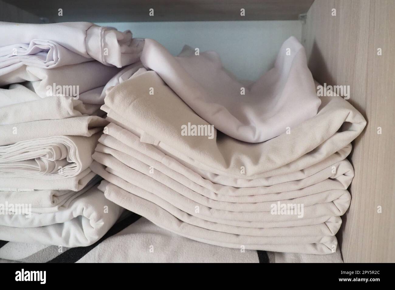 Les draps blancs sont empilés dans le placard. Contenu interne d'une armoire à linge. Organisation du ménage. Conditions d'hygiène pour le sommeil. Tissus et draps dans un placard ou une armoire blanc à moitié ouvert Banque D'Images