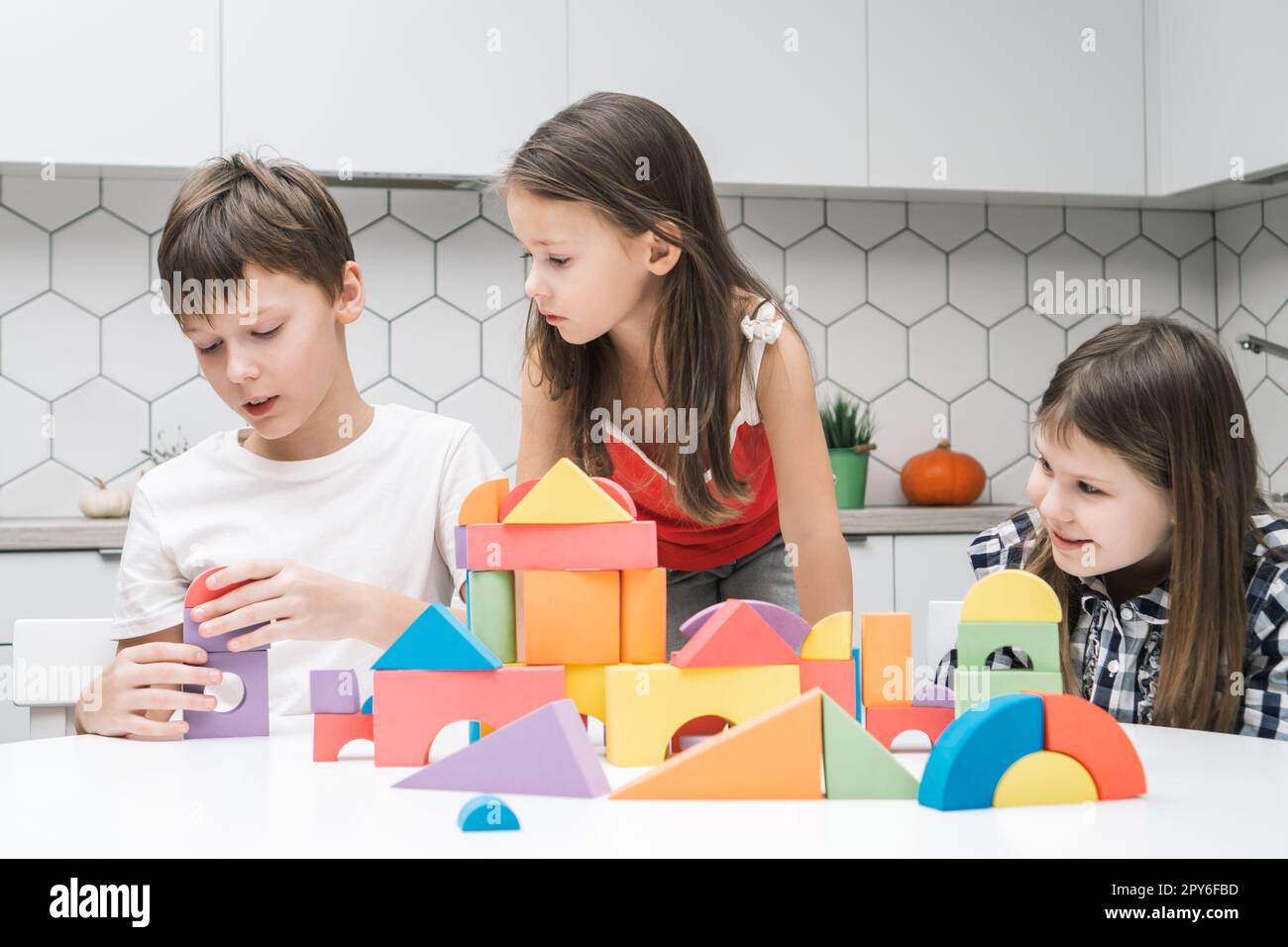 Les petits amis jouent le constructeur sur la table. Les filles regardent garçon collectent des détails colorés de lego. Les enfants construisent une ville de jouets. Banque D'Images