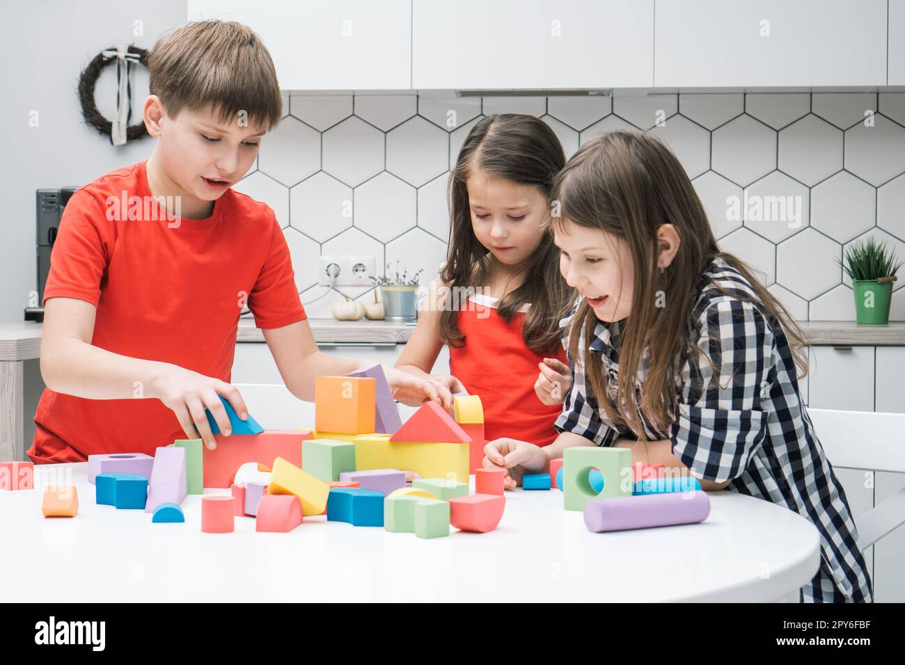 Drôle d'amis d'école jouent constructeur sur la table de cuisine. Les filles et les garçons collectent des détails colorés de lego, construisent la ville des jouets. Banque D'Images