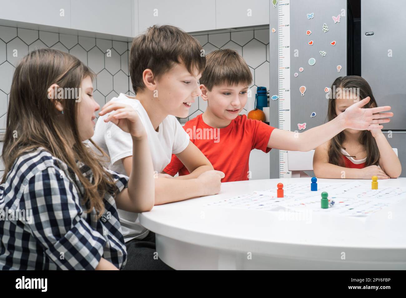 Des amis de petite école joyeux jouent à un jeu de société sur une carte papier avec des dés et des jetons à la table, vue latérale. Jeu de table intéressant Banque D'Images