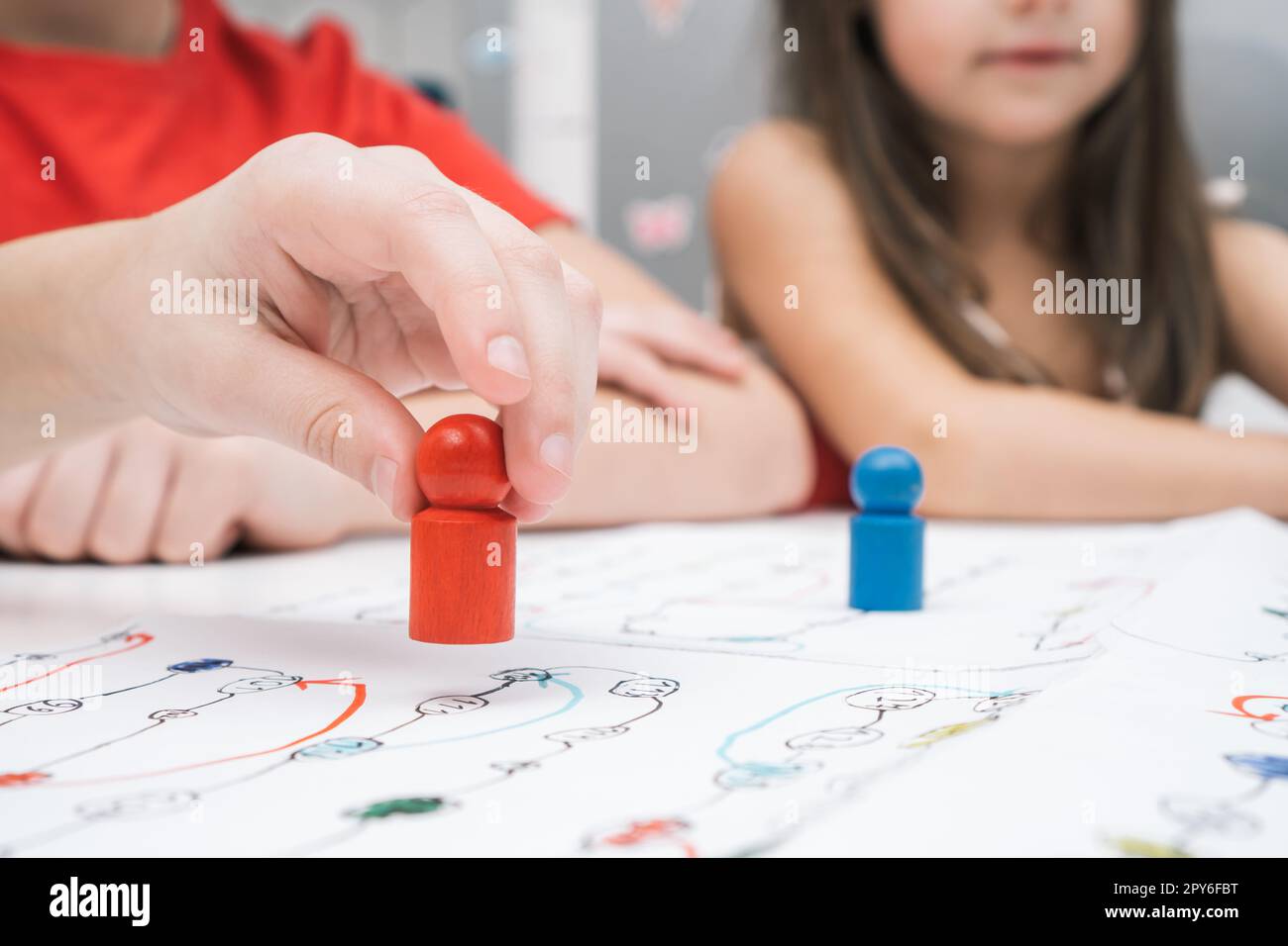 Les petits amis jouent à un jeu de société sur une carte papier à table. Main du joueur tenir la figure rouge gros plan, mise au point sélective. Banque D'Images