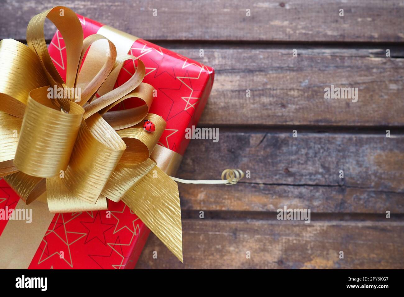 Boîte cadeau rouge avec grand noeud doré sur fond de bois. Cadeau de Noël, nouvel an, anniversaire, Fête des mères, mariage, Saint Valentin. Belle décoration de fête. Noeud luxuriant en ruban jaune. Banque D'Images