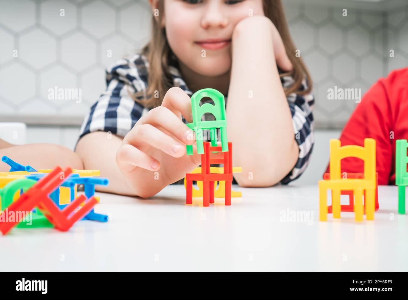 Petite école fille jouer jouet chaises colorées assis à la table près. Portrait d'un enfant tenant de petits meubles en plastique. Banque D'Images