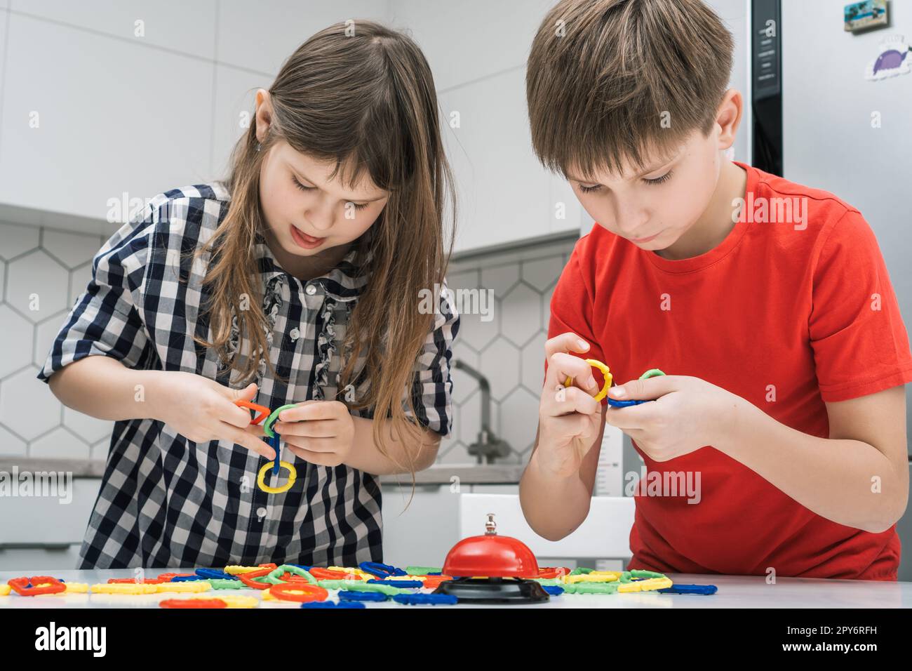 Les enfants jouent jouet constructeur debout au-dessus de la table de cuisine et regardant vers le bas. Garçon et fille collectent les détails colorés de lego. Banque D'Images