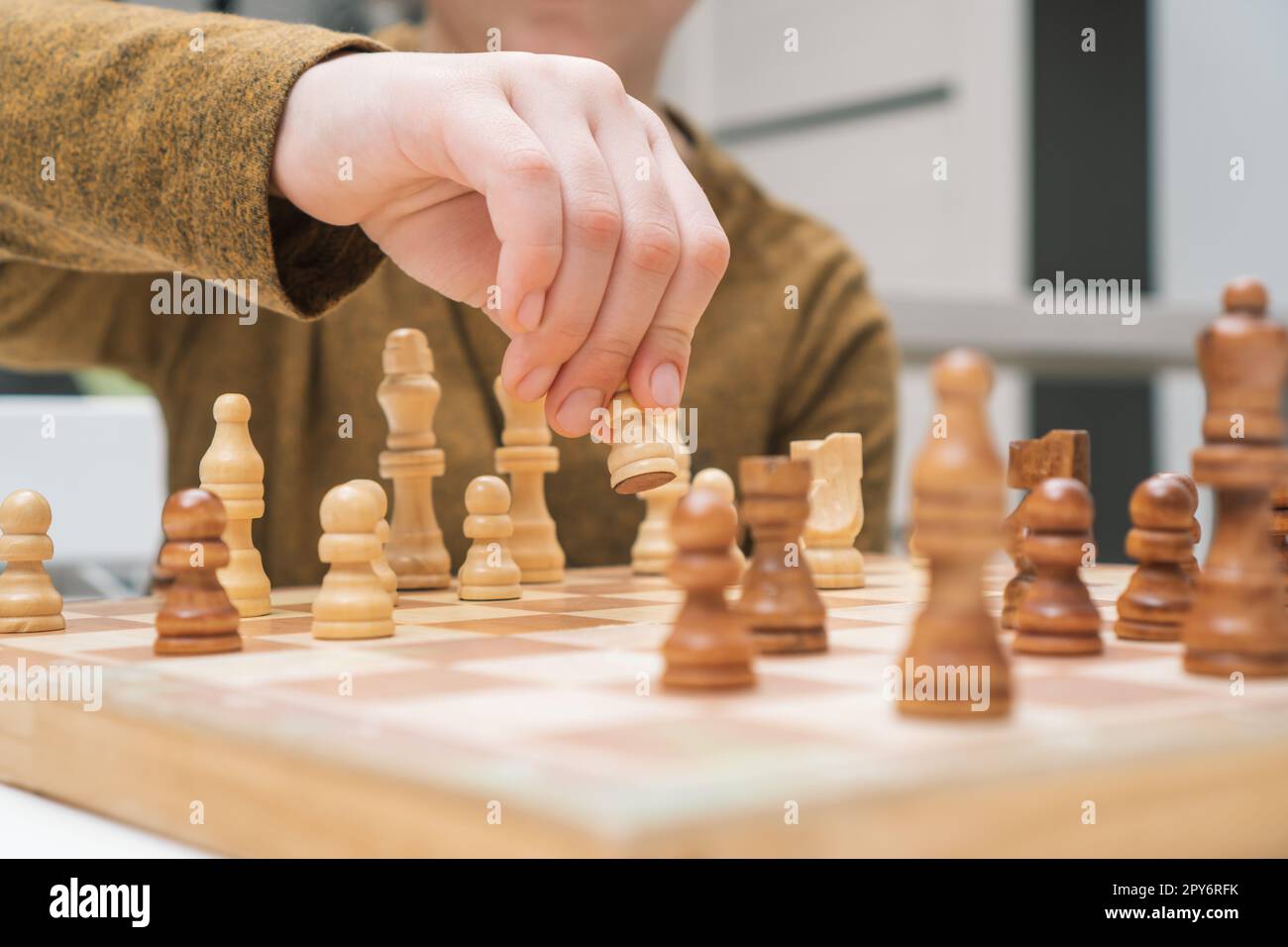 Un garçon joue aux échecs assis près de la table. Main de l'enfant déplacer le pion blanc sur l'échiquier en bois. Stratégie de jeu, tactiques. Banque D'Images