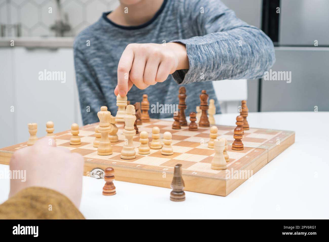 Les garçons jouent aux échecs assis à la table de cuisine. Main de l'enfant déplacer la figure blanche sur l'échiquier en bois. Stratégie de jeu, tactiques. Banque D'Images