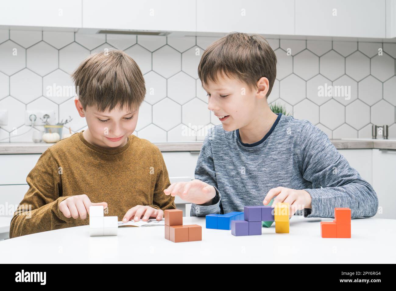 Les écoliers heureux jouent jouet constructeur assis à table. Les enfants collectent des détails colorés de lego, replient les figures de Tetris. Banque D'Images