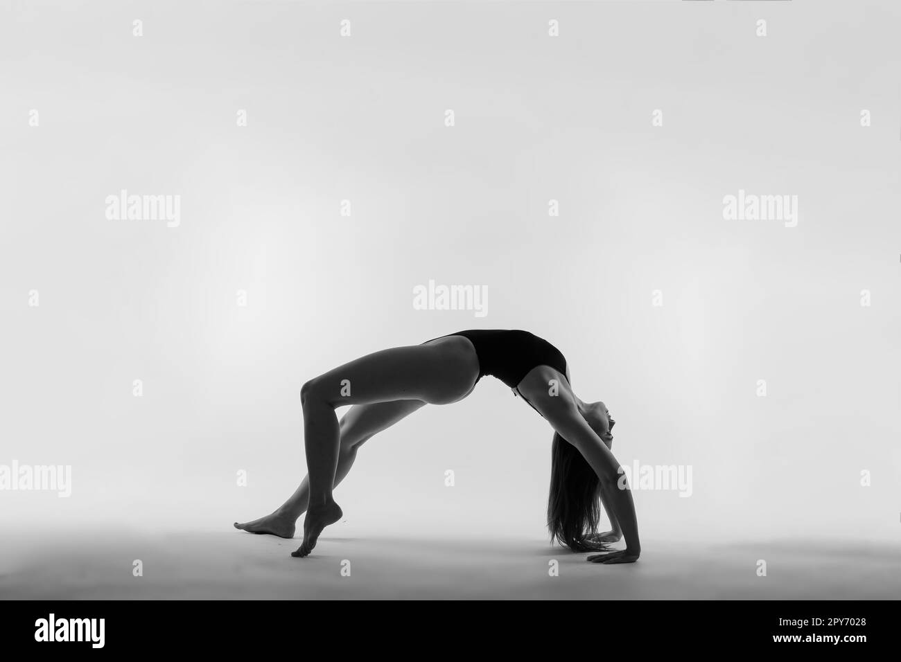 Jeune femme mince en body noir fait de l'exercice d'étirement de yoga sur fond blanc de mur de studio. Banque D'Images