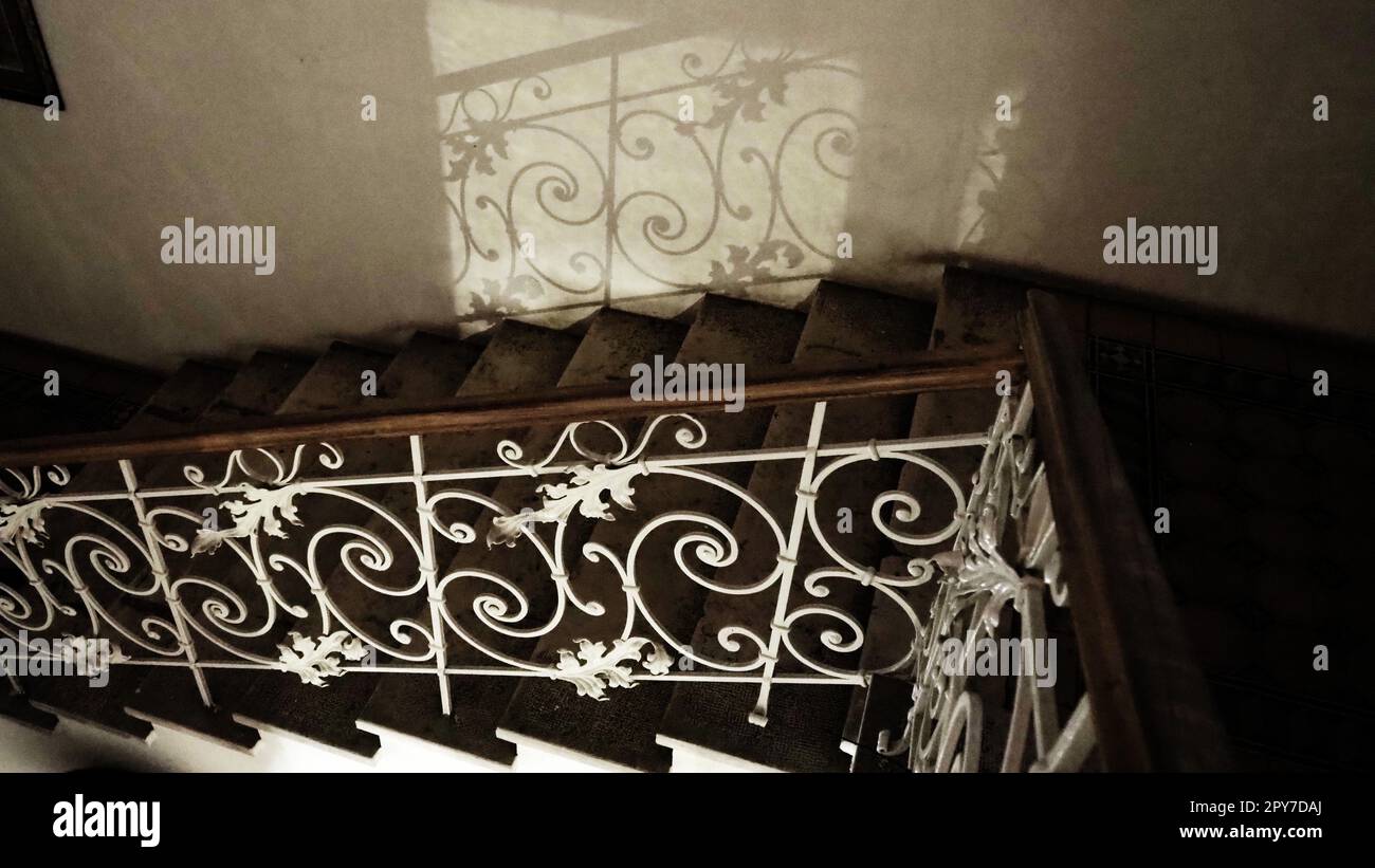 Escalier mystérieux avec une rambarde en métal forgé la nuit dans l'obscurité avec une faible lumière. Réflexion de curligues et de forgeage de motifs. Rambardes et marches. Escalier dans le musée Sremska Mitrovica Serbie Banque D'Images