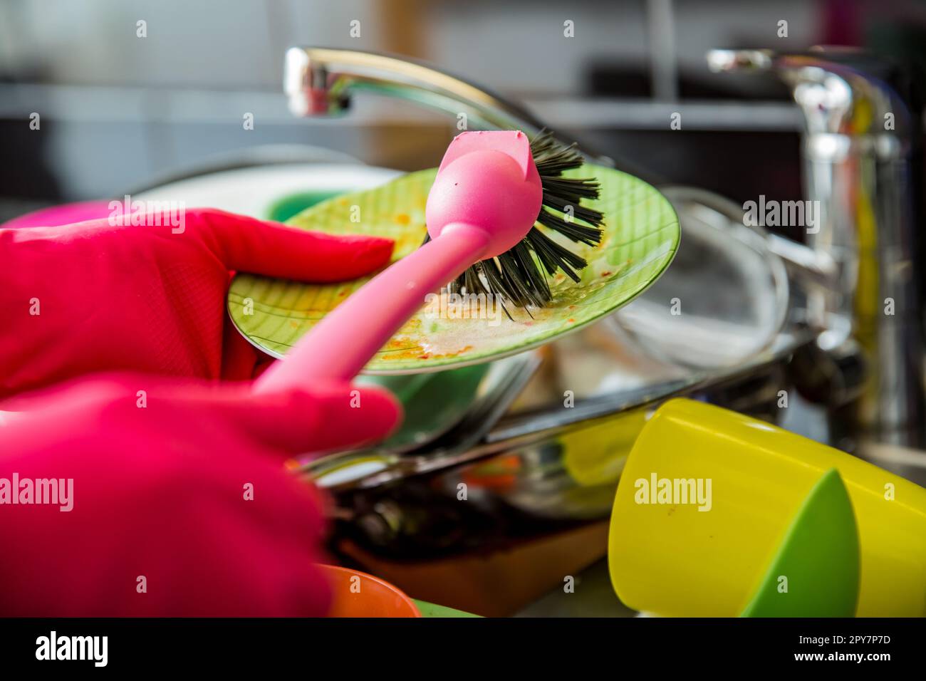 Évier de cuisine plein de vaisselle sale. Femme en gants de caoutchouc rose faisant la vaisselle, en utilisant la brosse. Comptoir de couleur sombre dans la cuisine moderne. Corvées de maison Banque D'Images