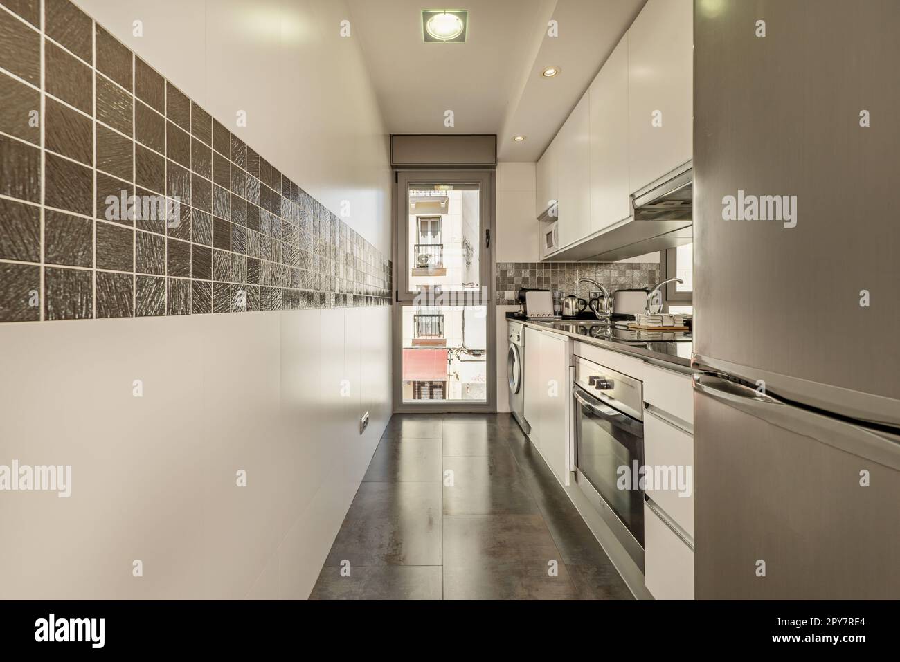 Une cuisine dans une pièce étroite avec une fenêtre du sol au plafond et une cantonnière de carreaux gris brillant Banque D'Images