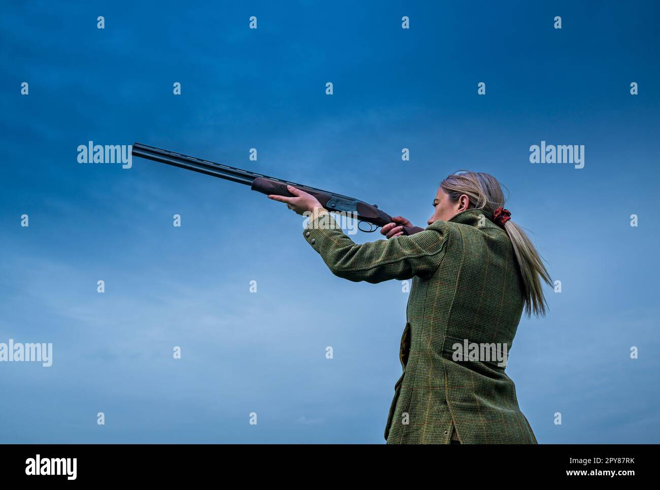 Un portrait d'une femme avec un fusil de chasse contre un ciel bleu Banque D'Images